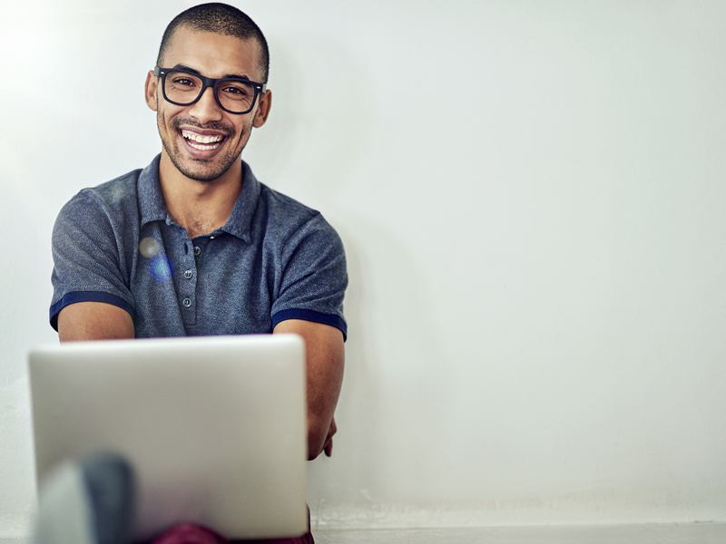 Smiling young professional seated on the floor with a laptop.